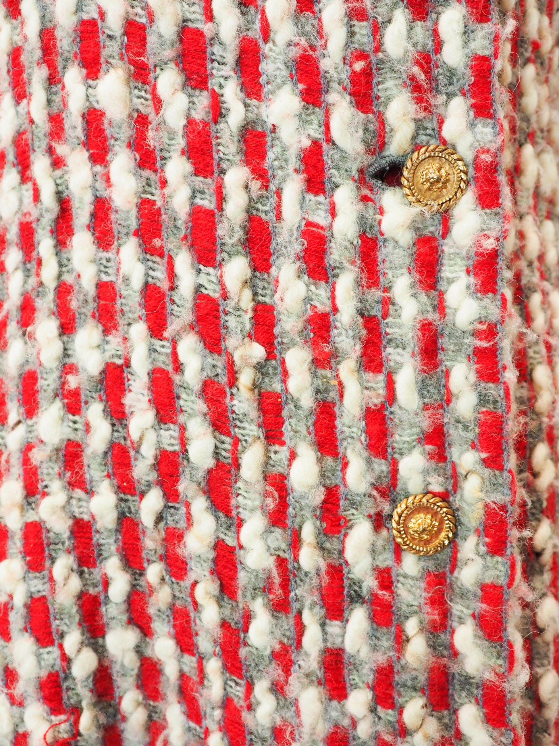 Close-up of a textured fabric with red, gray, and white pattern and gold buttons.