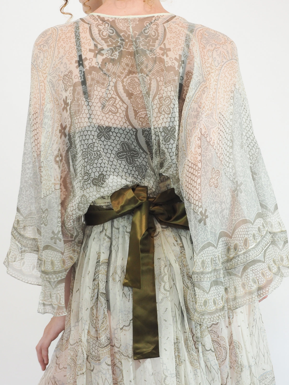 A vintage Zandra Rhodes long sheer maxi dress with a print detailing, wide three-quarter sleeves, and a wide dark olive green belt at the waist