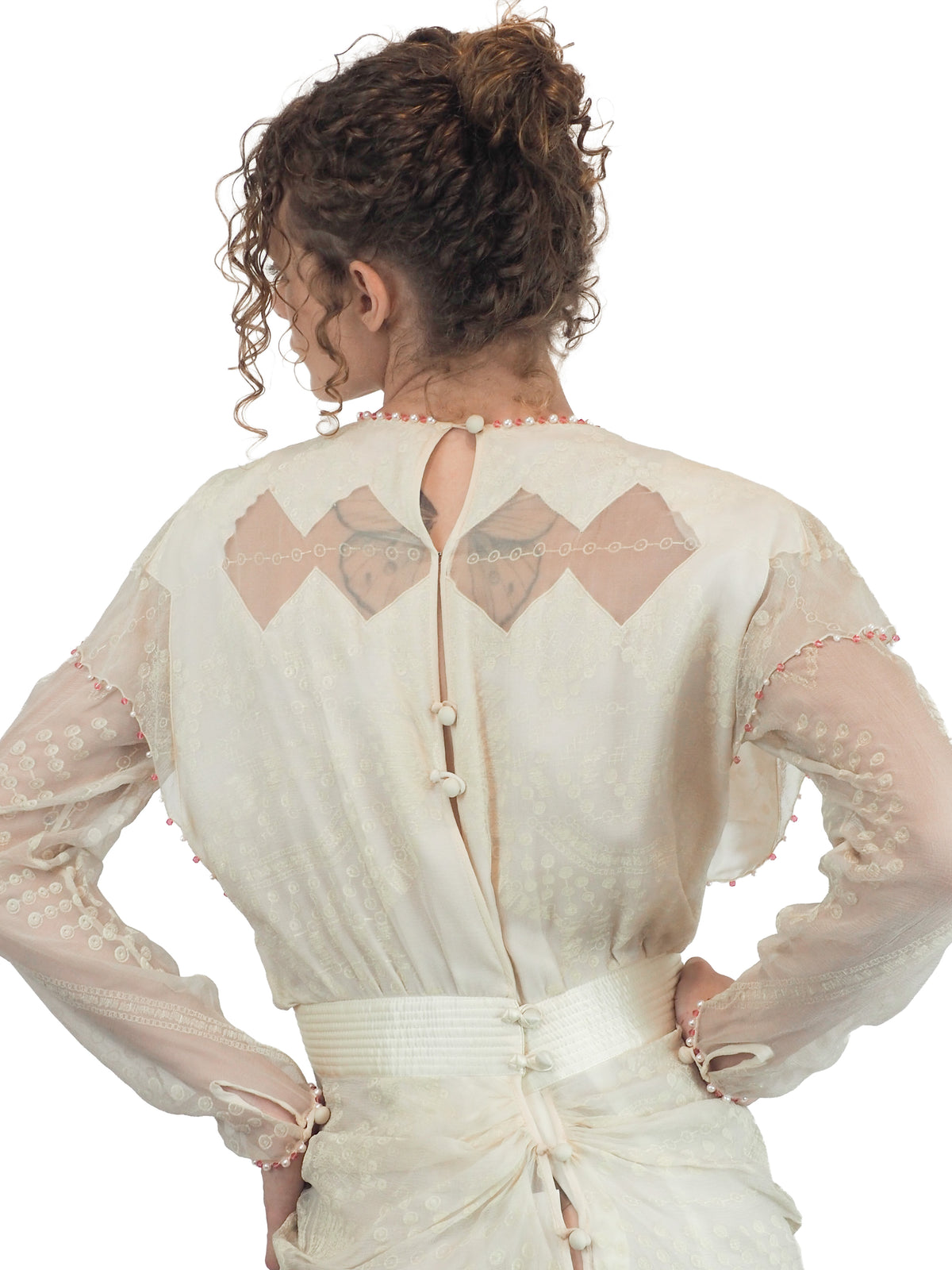 A vintage Zandra Rhodes cream-colored bridal wedding dress with sheer long sleeves, pink beaded detailing, a gathered waist, and a draped skirt