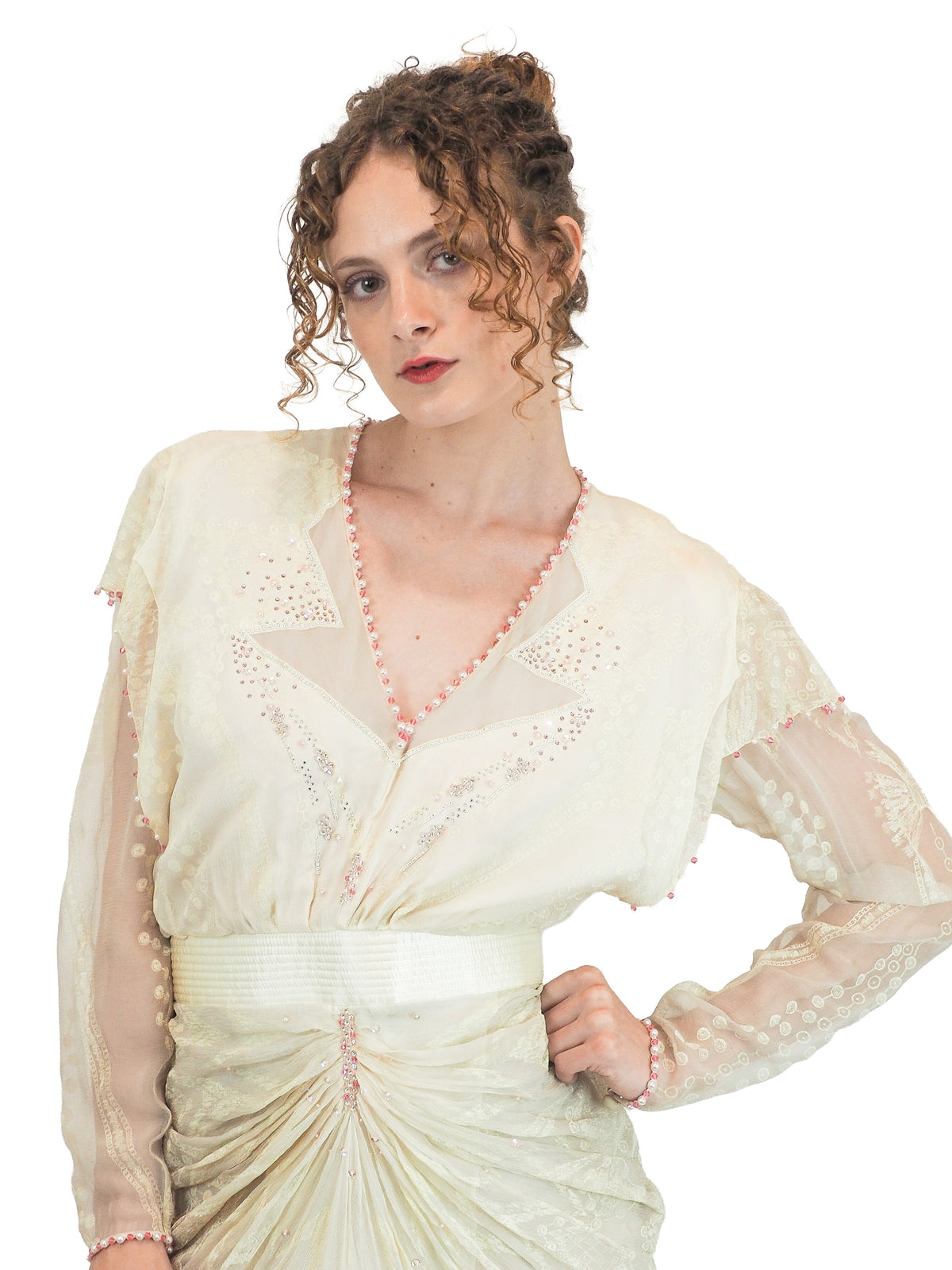 A vintage Zandra Rhodes cream-colored bridal wedding dress with sheer long sleeves, pink beaded detailing, a gathered waist, and a draped skirt