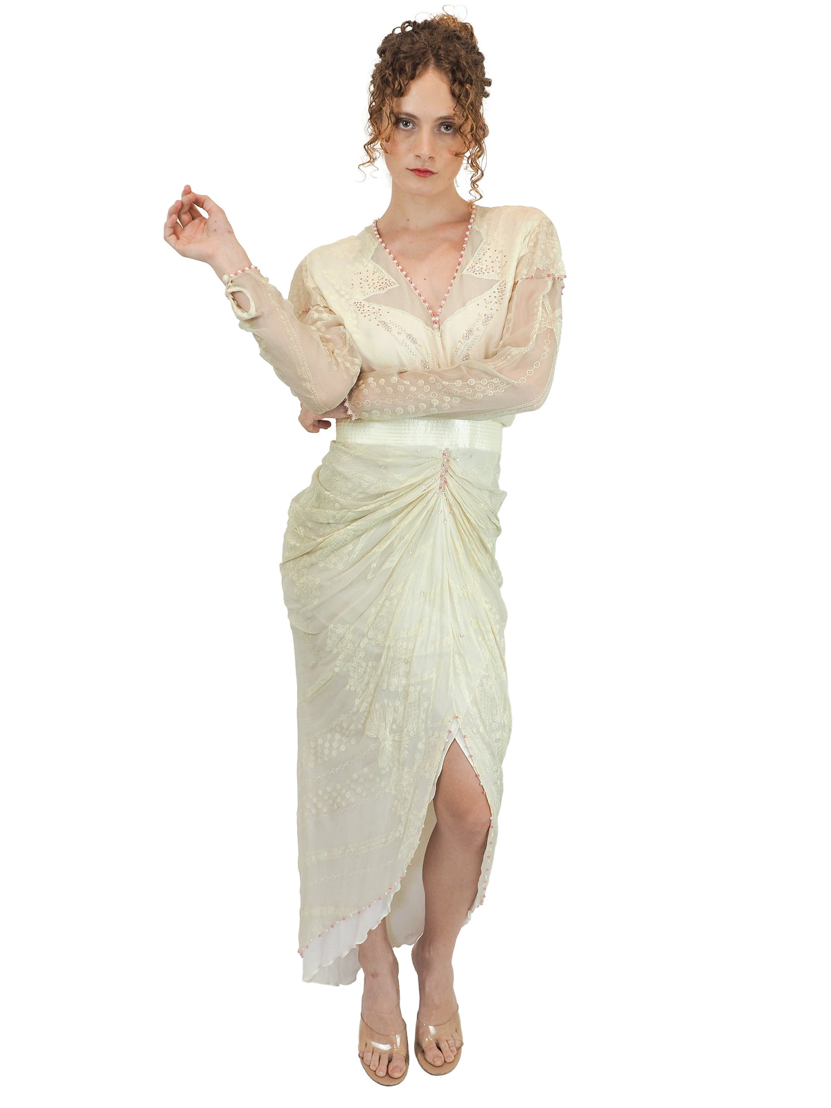 A vintage Zandra Rhodes cream-colored bridal wedding dress with sheer long sleeves, pink beaded detailing, a gathered waist, and a draped skirt