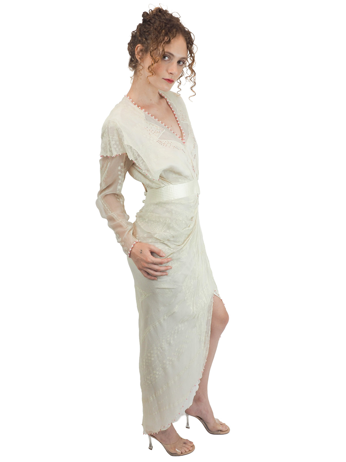 A vintage Zandra Rhodes cream-colored bridal wedding dress with sheer long sleeves, pink beaded detailing, a gathered waist, and a draped skirt
