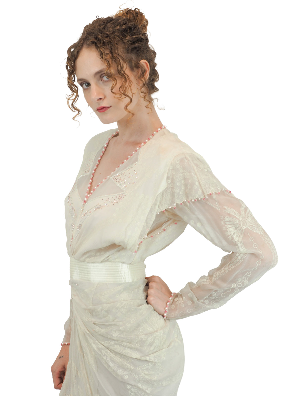 A vintage Zandra Rhodes cream-colored bridal wedding dress with sheer long sleeves, pink beaded detailing, a gathered waist, and a draped skirt
