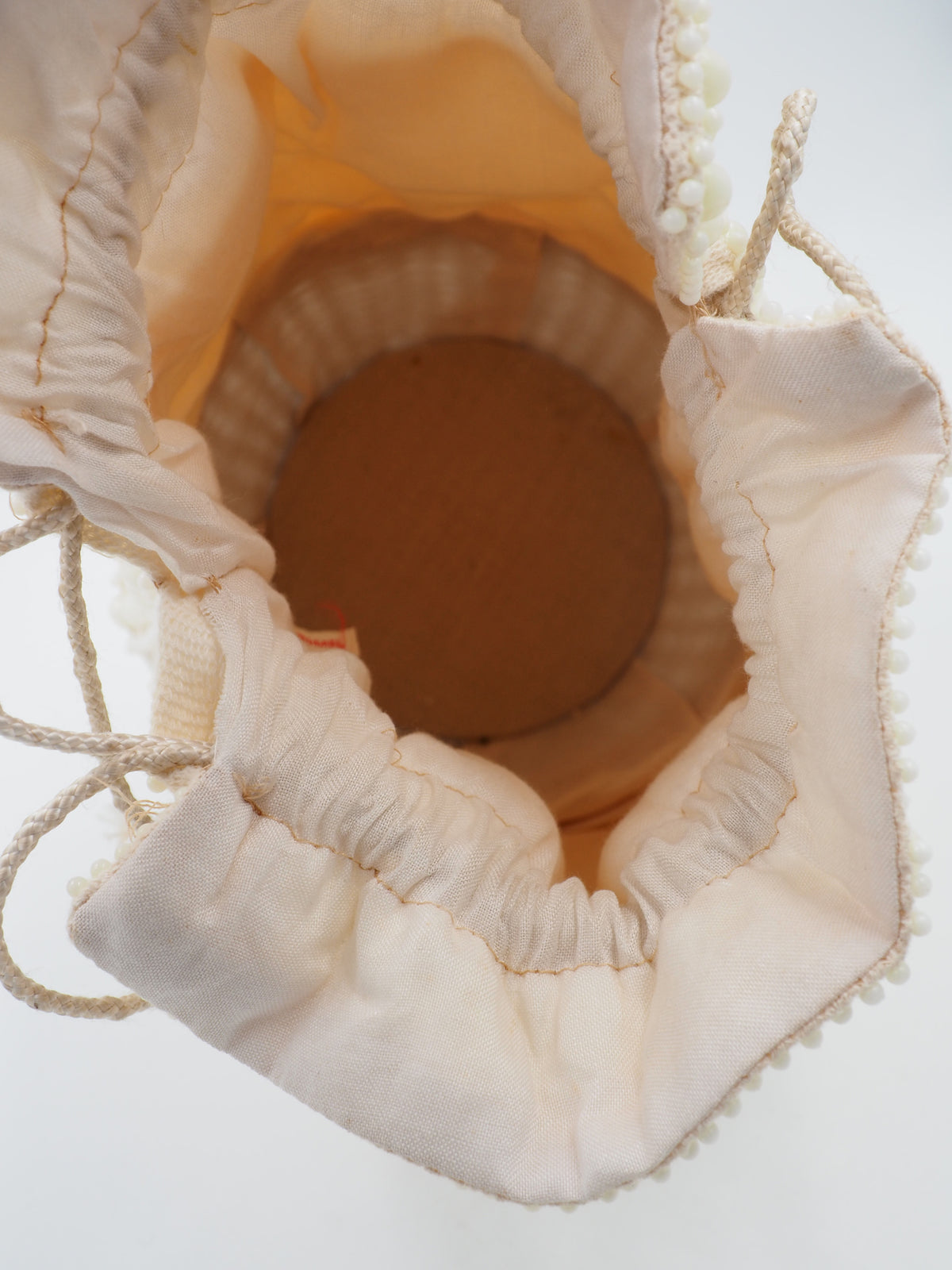 A cream-colored beaded bucket bag with a textured pom-pom pattern, featuring a drawstring closure and a light white woven basket base