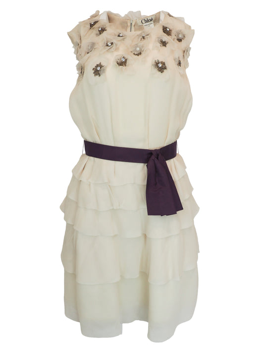 A vintage Chloe Y2K off-white sleeveless ruffled dress with floral embellishments on the bodice and a dark purple waist belt 