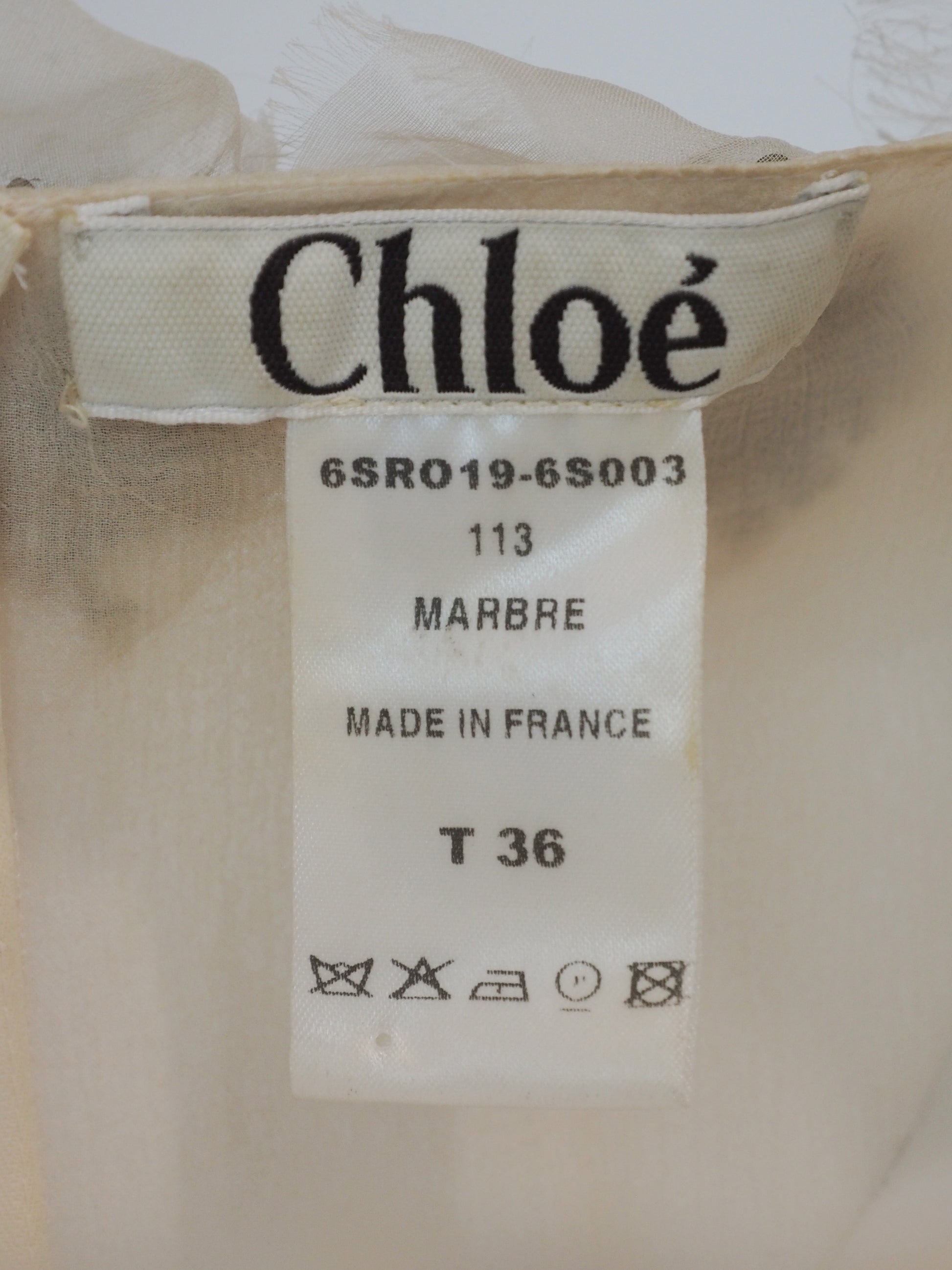 A vintage Chloe Y2K off-white sleeveless ruffled dress with floral embellishments on the bodice and a dark purple waist belt 