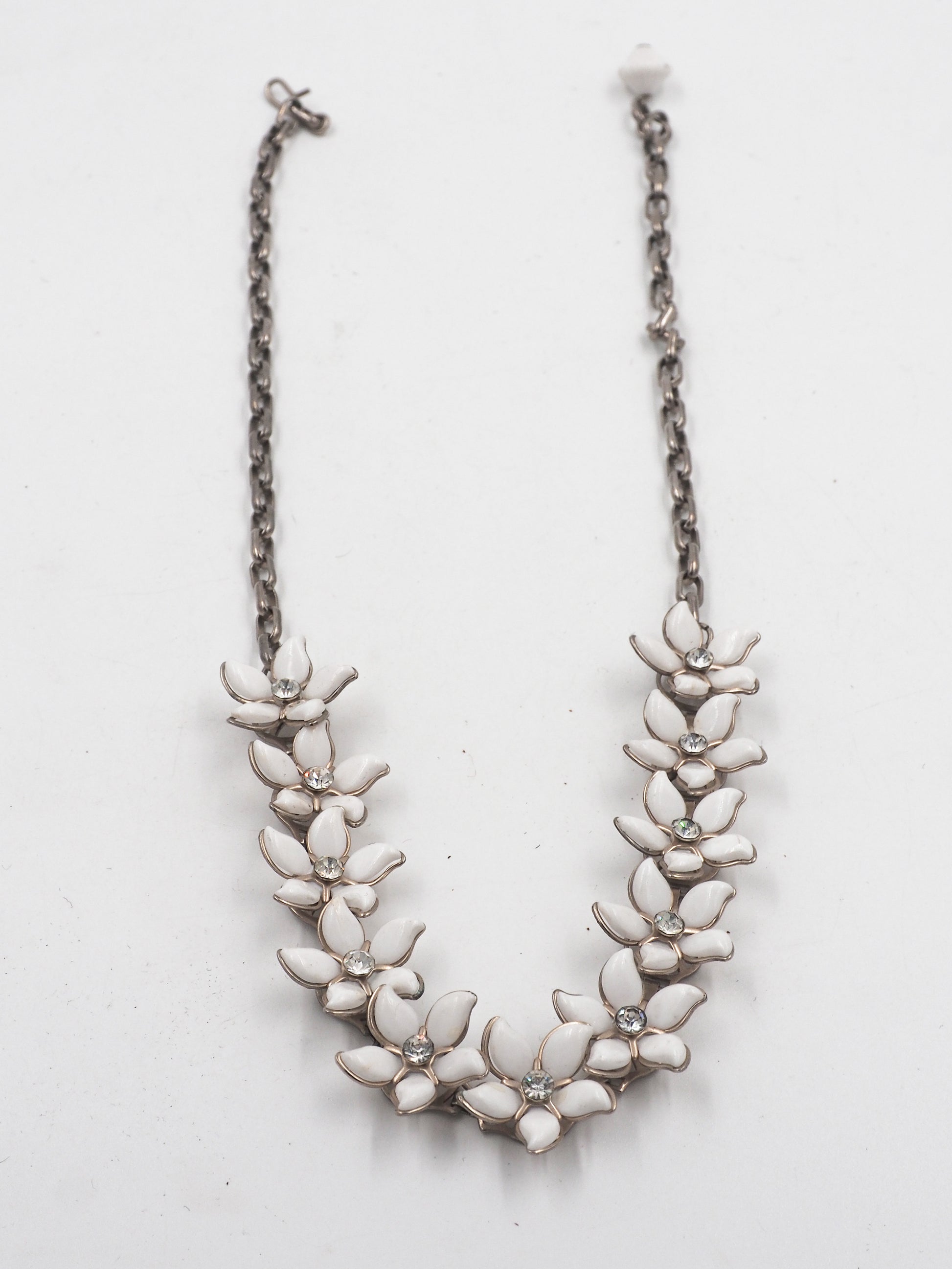 A vintage bridal silver-tone chain necklace featuring a row of white enamel flower blossoms with small clear rhinestone accents