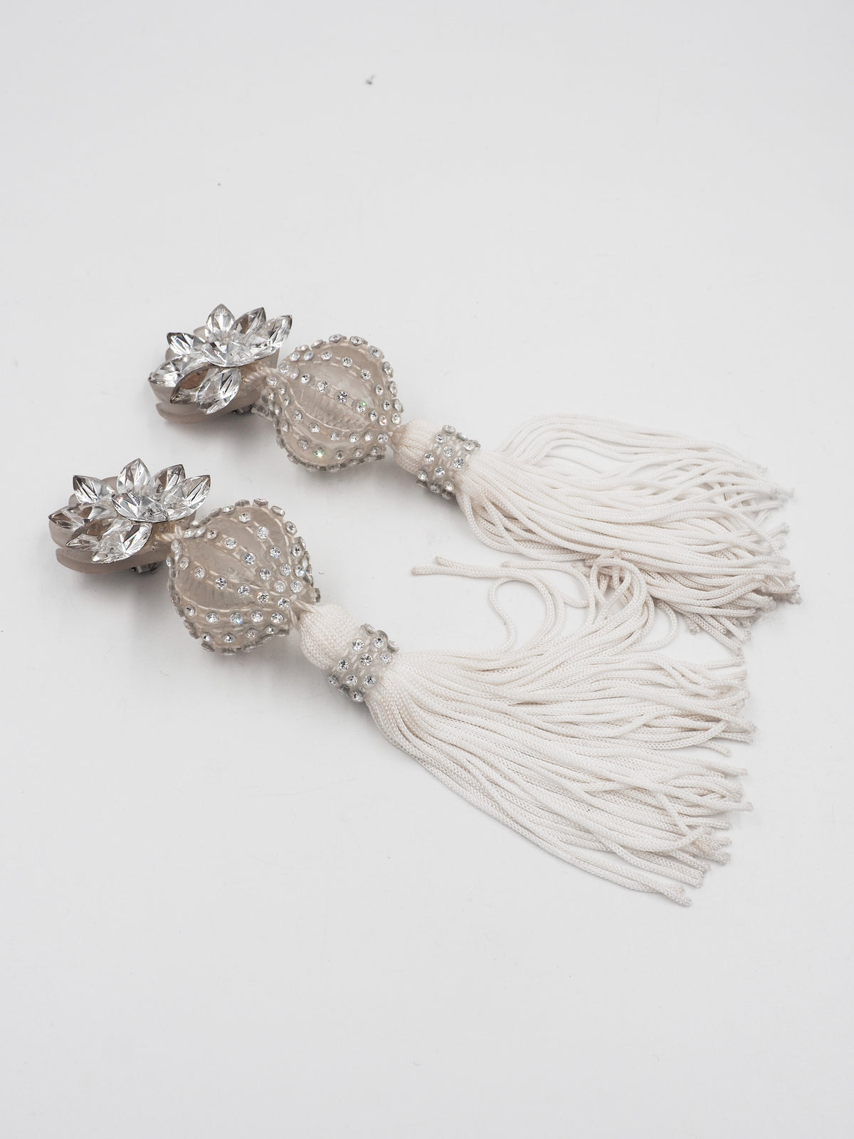 A pair of long, ornate drop earrings with clear faceted crystal flower tops, cream beadwork, and long cream tassel fringe