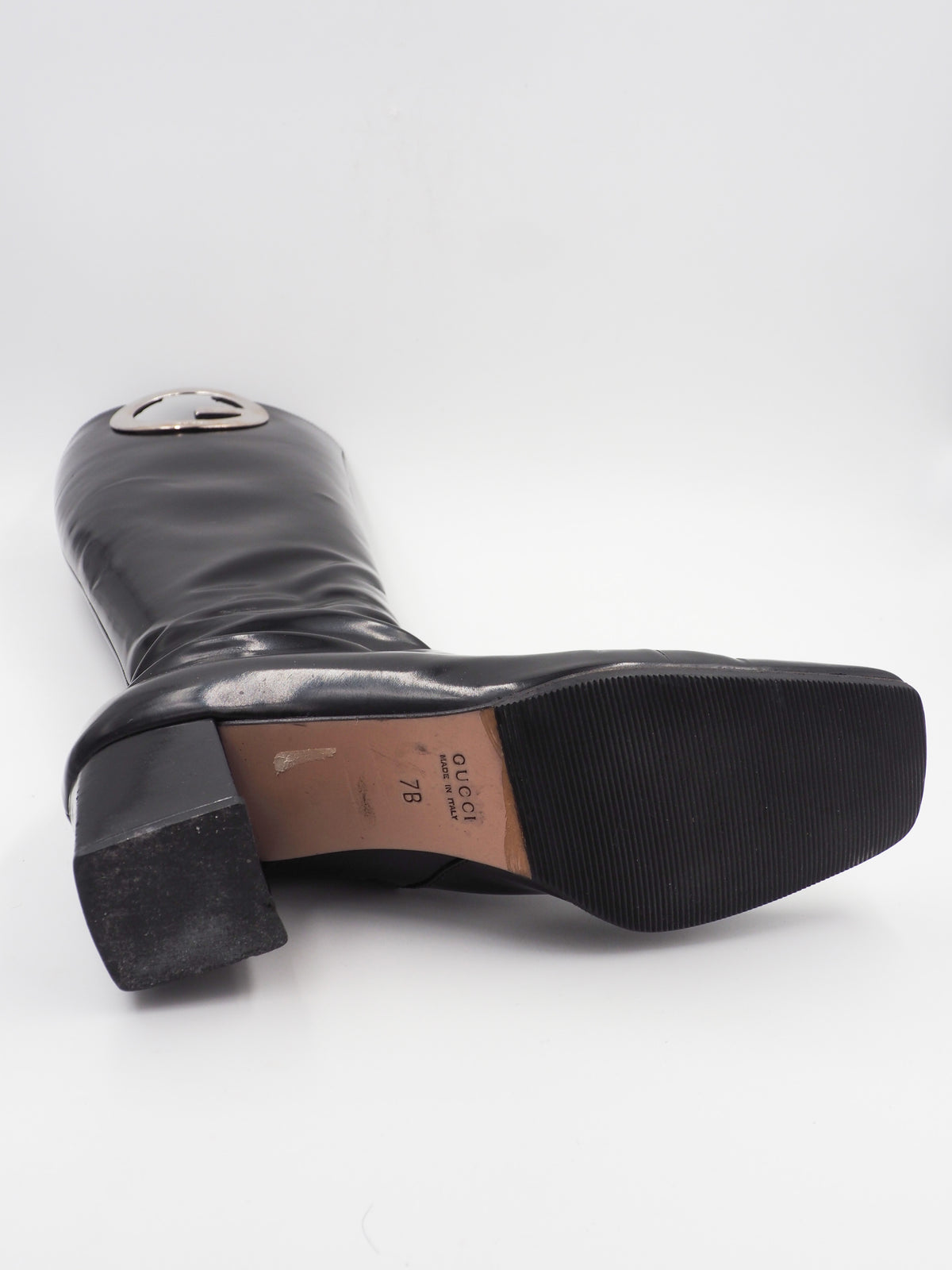 A vintage gucci 1990s black leather knee-high boot with a chunky block heel and a large circular silver-tone metal ring logo detail near the top shaft