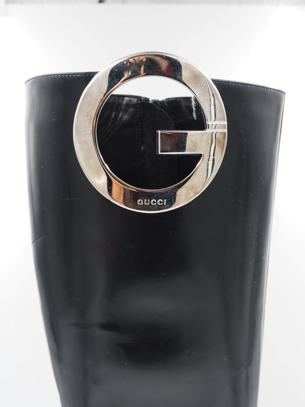 A vintage gucci 1990s black leather knee-high boot with a chunky block heel and a large circular silver-tone metal ring logo detail near the top shaft