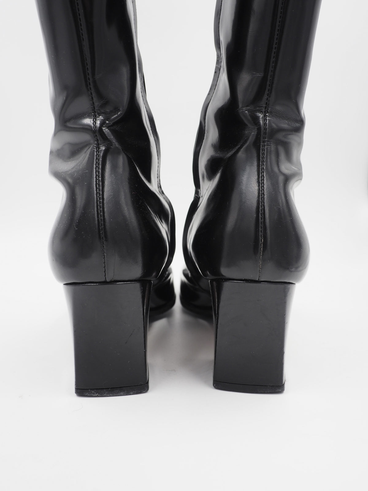 A vintage gucci 1990s black leather knee-high boot with a chunky block heel and a large circular silver-tone metal ring logo detail near the top shaft