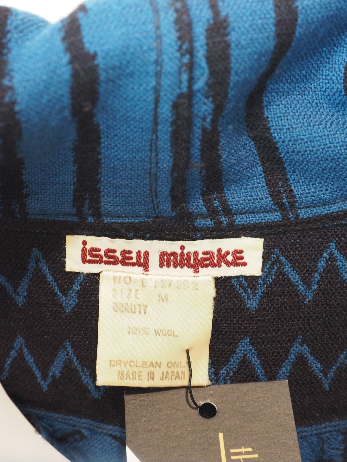 A vintage Issey Miyake long-sleeve, high-neck tunic top featuring a blue and black geometric pattern with fringed edges