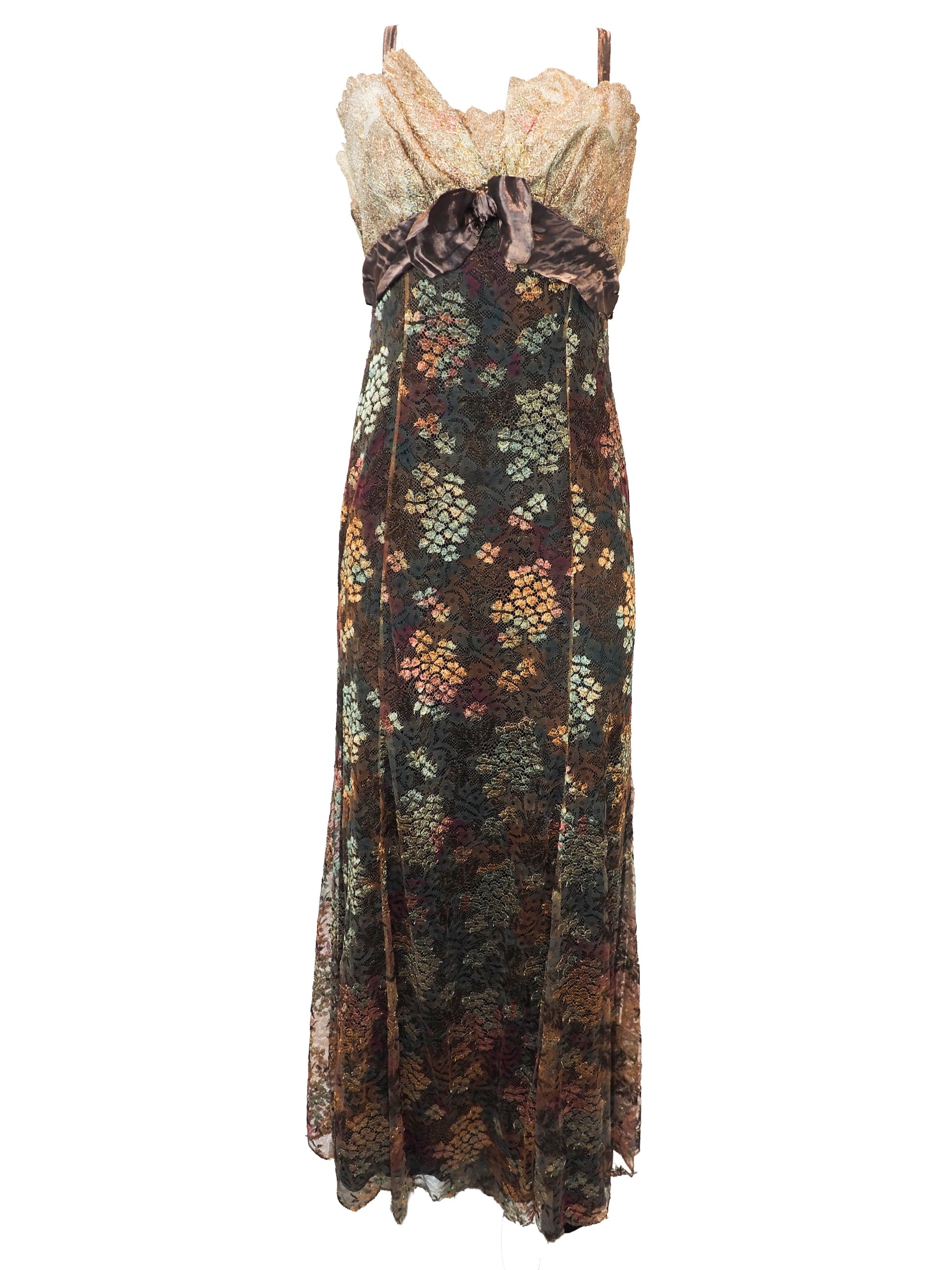 A vintage christian Lacroix runway sleeveless maxi dress with a sheer floral lace pattern in earthy tones of brown, green, and gold, featuring a cream lace bodice and a dark brown satin waist tie
