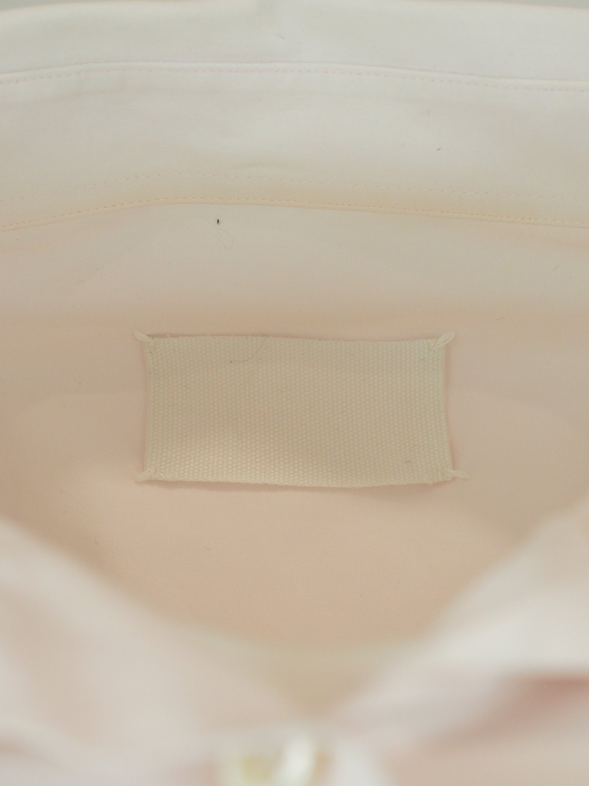 A vintage Maison Martin margiela 2001 pale blush pink oversized button-down shirt dress with a pointed collar, long sleeves, and a small black embroidered clover on the left chest