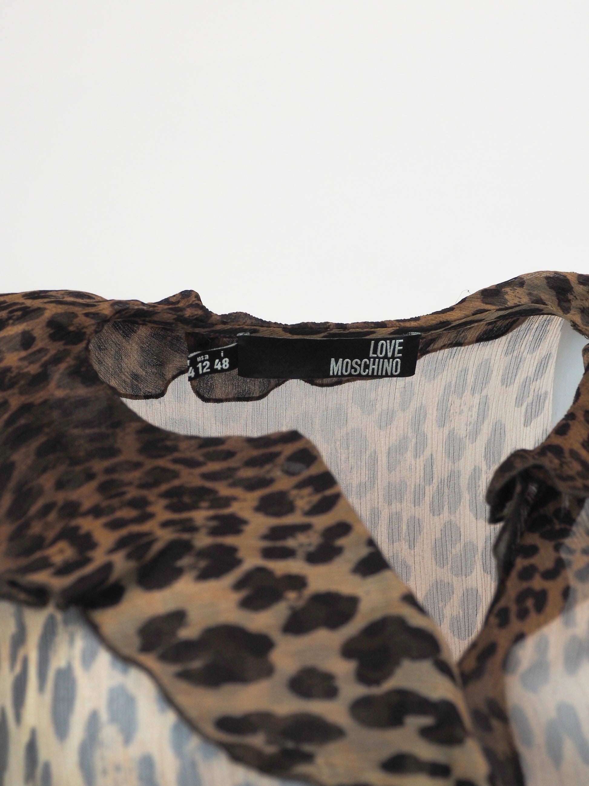 A vintage moschino sheer leopard-print blouse with a ruffled collar, button-front center panel, and matching ruffled cuffs