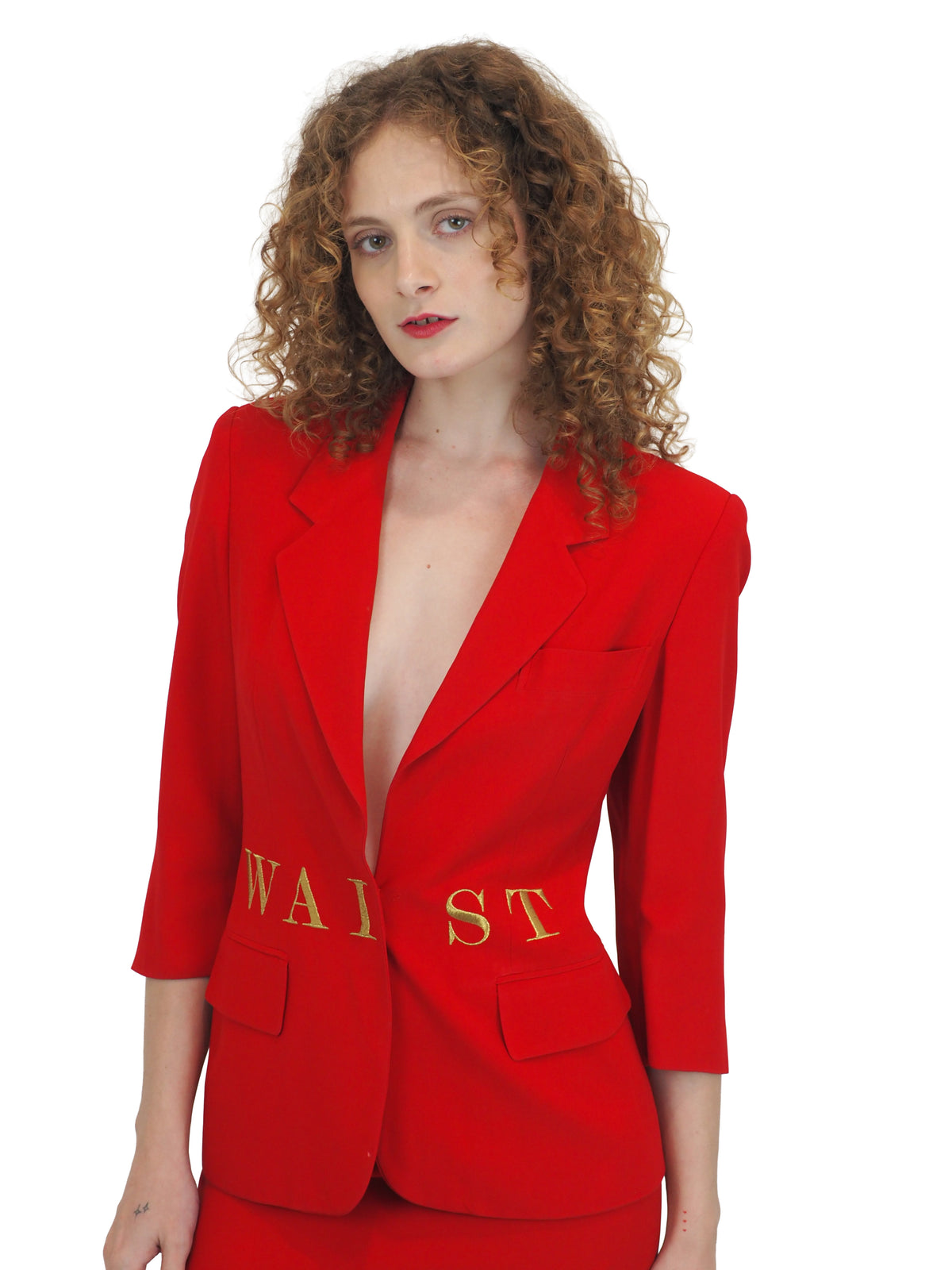 A vintage 1991 moschino bright red two-piece suit with gold lettering reading "waist of money"