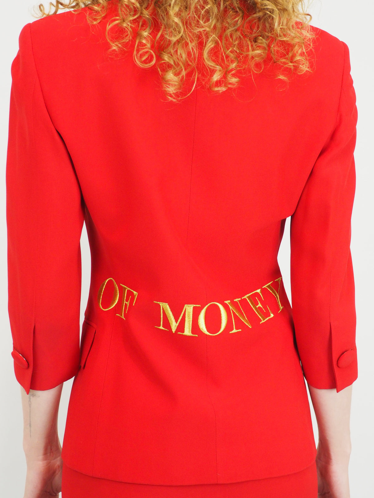 A vintage 1991 moschino bright red two-piece suit with gold lettering reading "waist of money"
