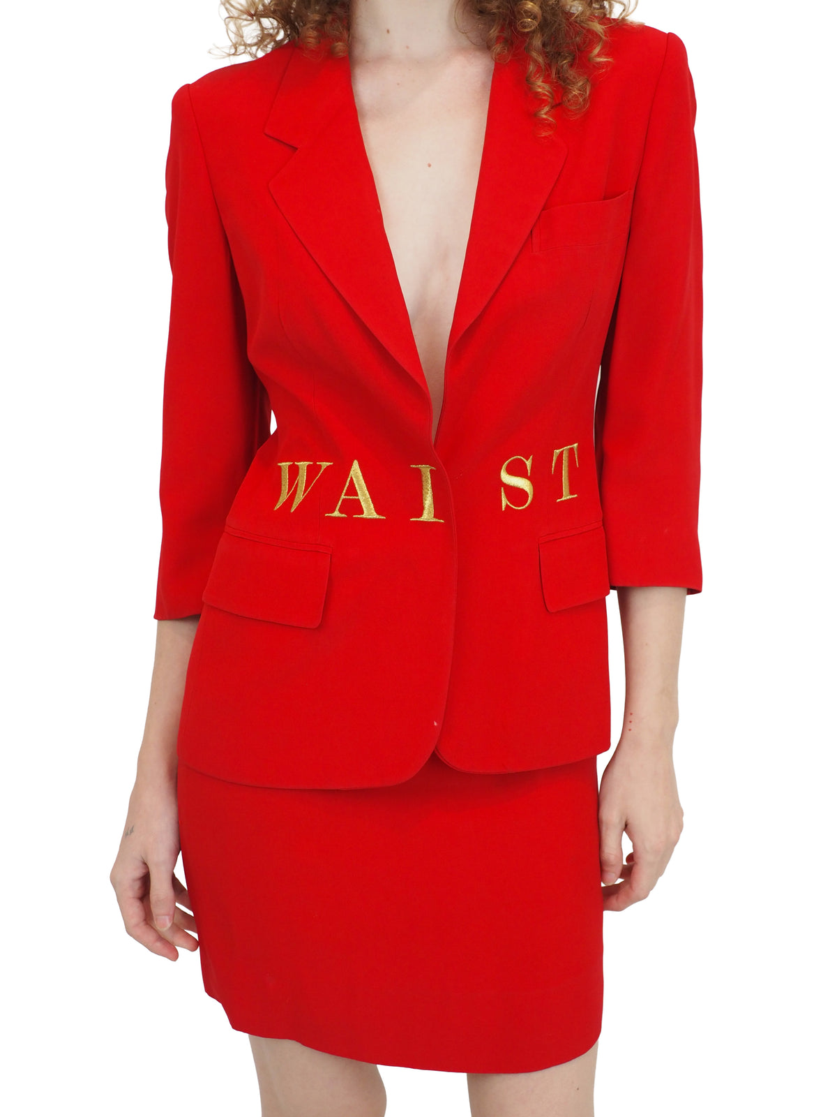 A vintage 1991 moschino bright red two-piece suit with gold lettering reading "waist of money"