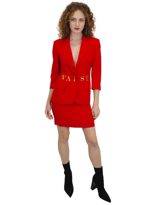 A vintage 1991 moschino bright red two-piece suit with gold lettering reading "waist of money"