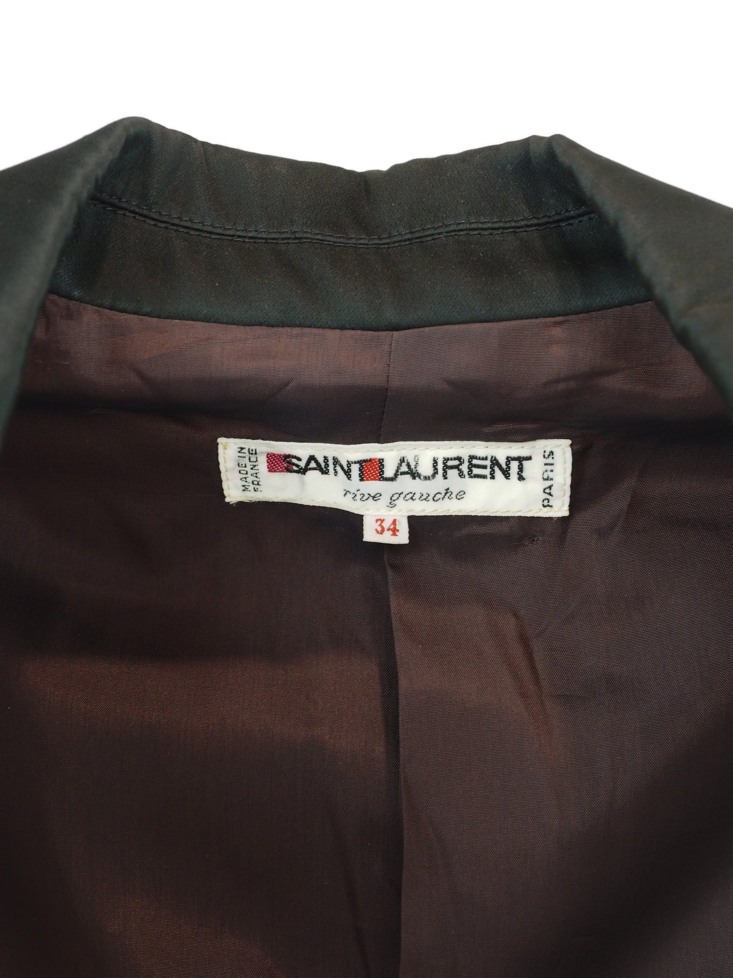 Close-up of the collar and inner neck of a Saint Laurent shirt, showing the dark olive green outer fabric, dark brown satin-like lining, and the white brand label with 'Saint Laurent' and 'rive gauche' printed on it.