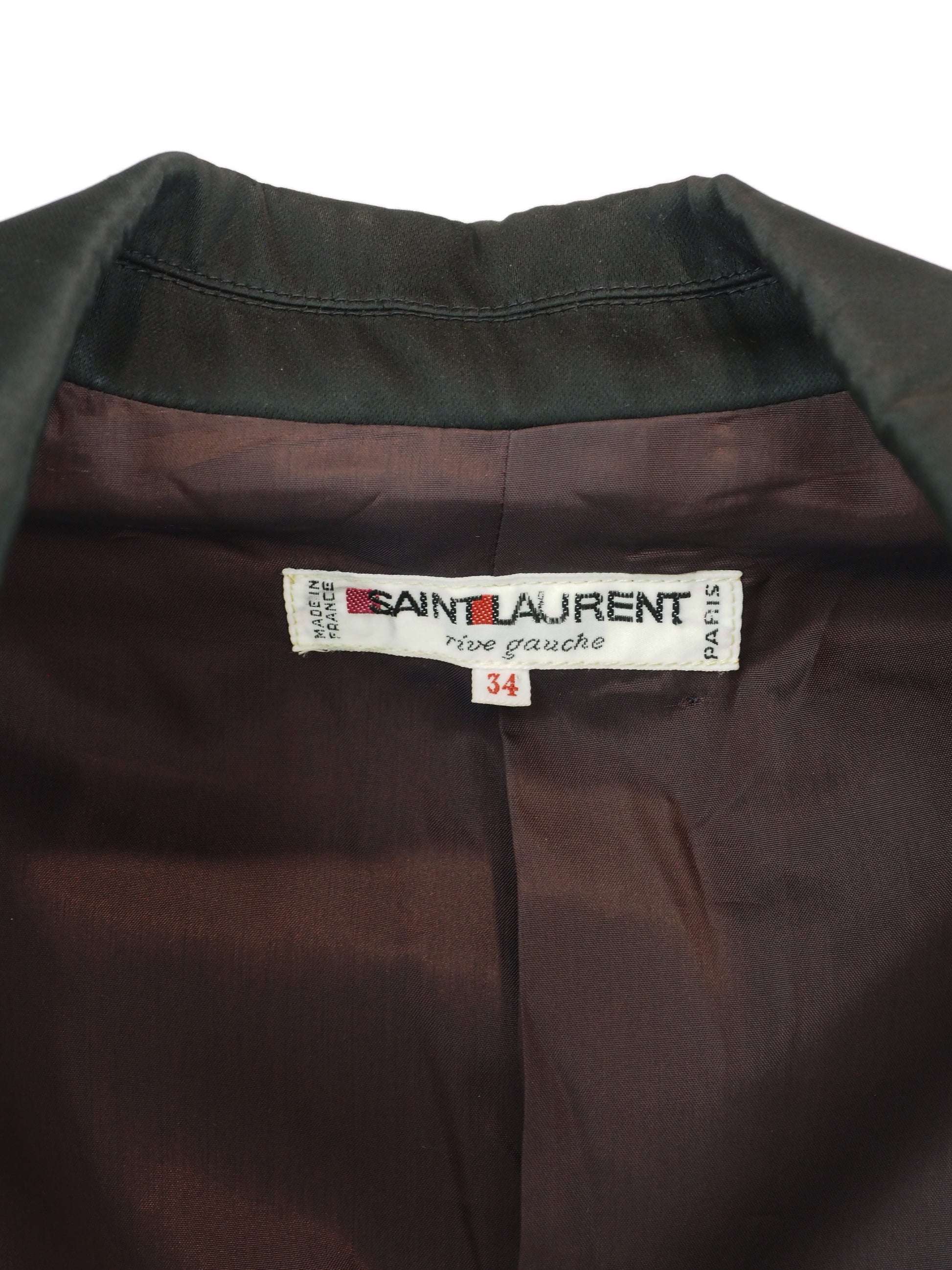 Close-up of the collar and inner neck of a Saint Laurent shirt, showing the dark olive green outer fabric, dark brown satin-like lining, and the white brand label with 'Saint Laurent' and 'rive gauche' printed on it.