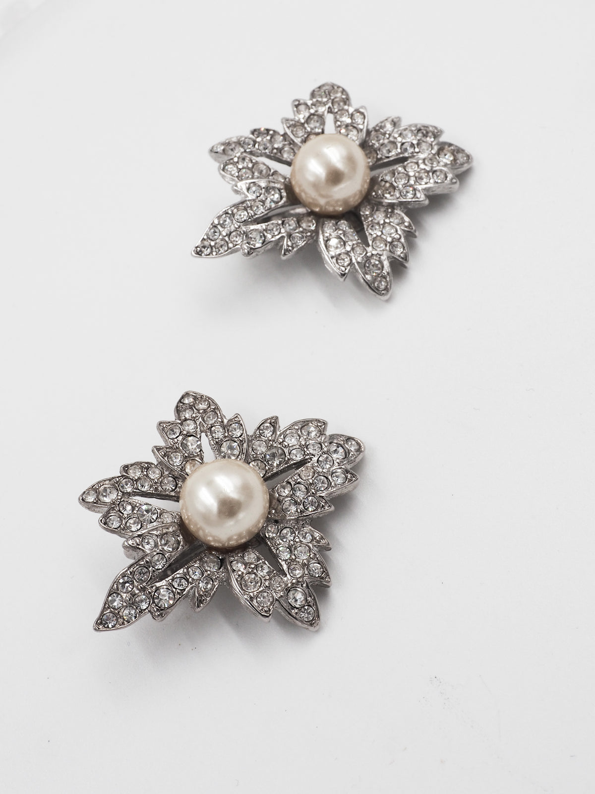 A pair of silver-toned leaf-shaped earrings with a central white pearl and pavé-set dark stones