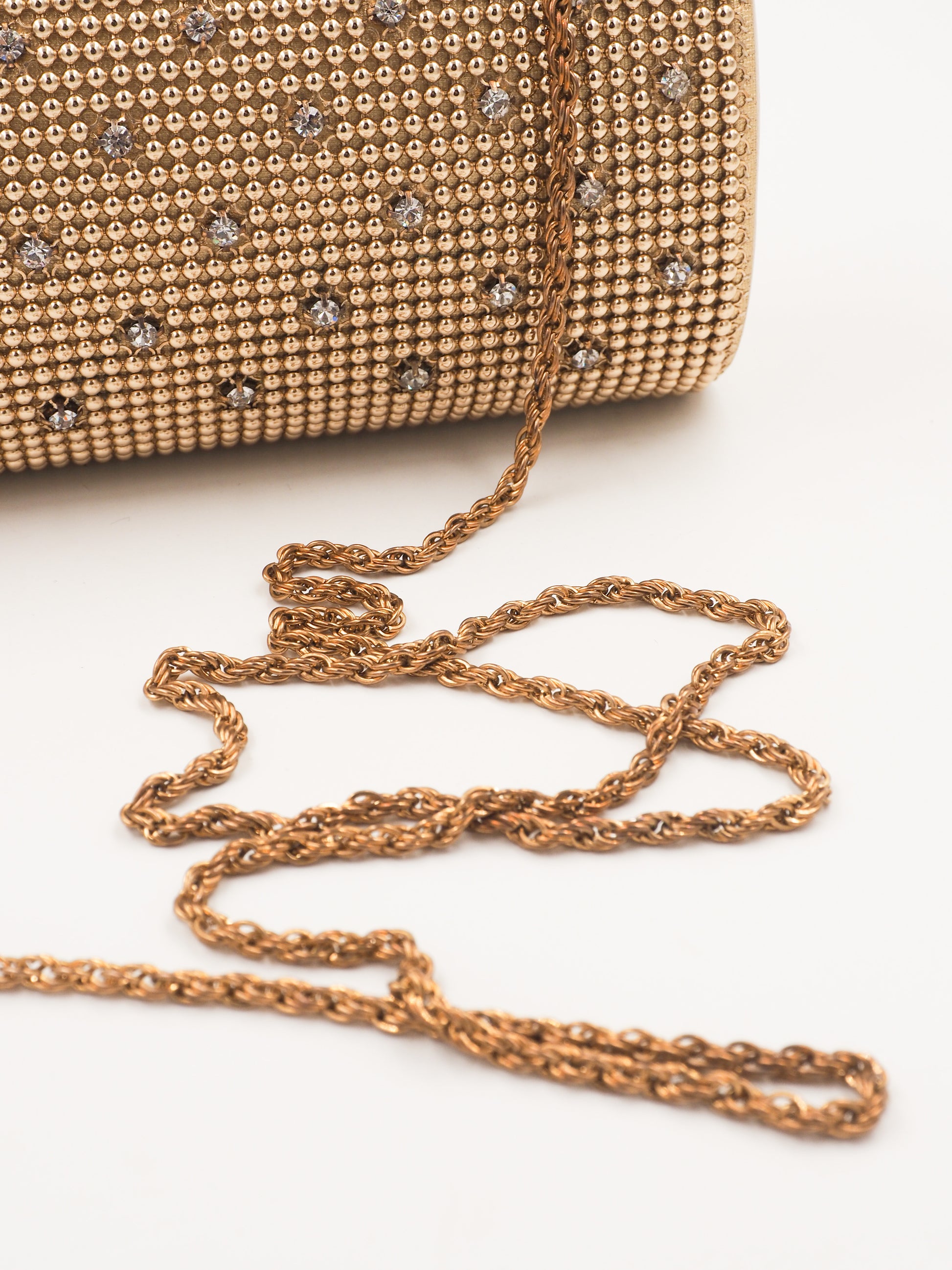 A whiting and davis gold-toned metallic clutch bag covered in a dense mesh of small rhinestones, decorated with a grid pattern of silver crystal studs